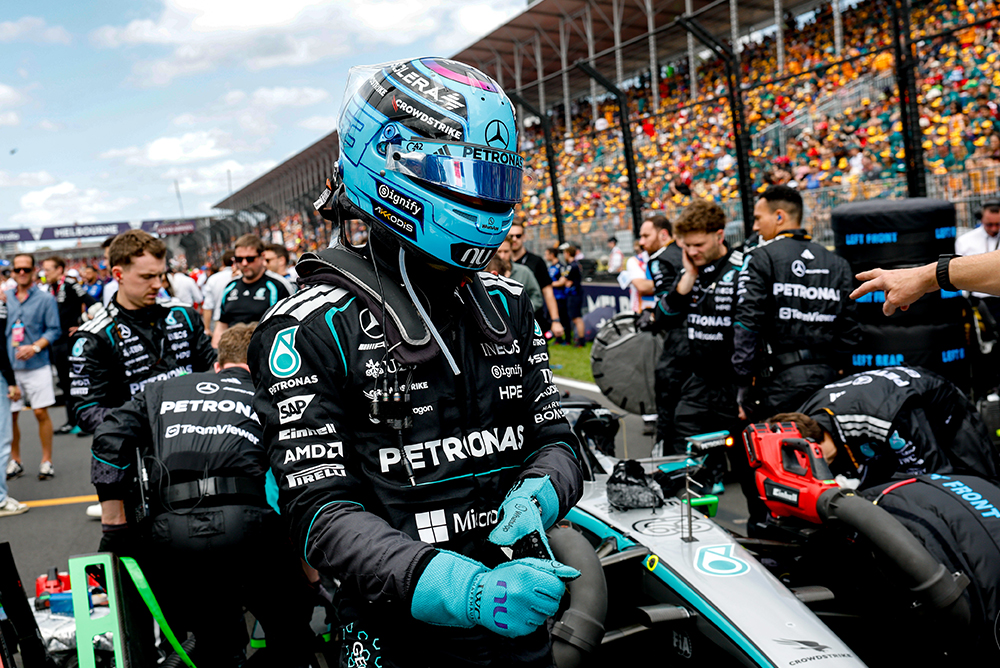 Formula 1 driver sitting in the race car on the starting grid with team in the background.