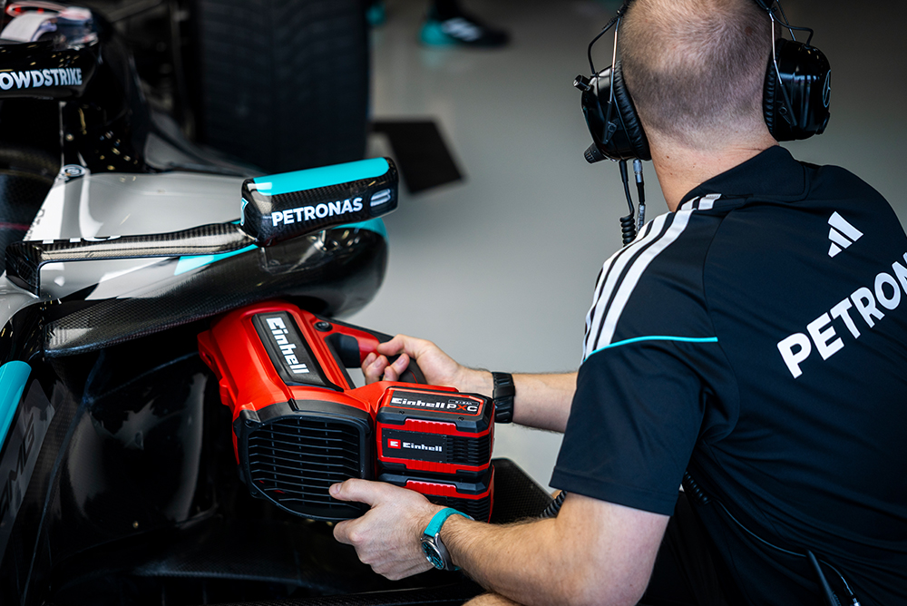 Formula 1 mechanic working with a tool on a race car in the pit lane.